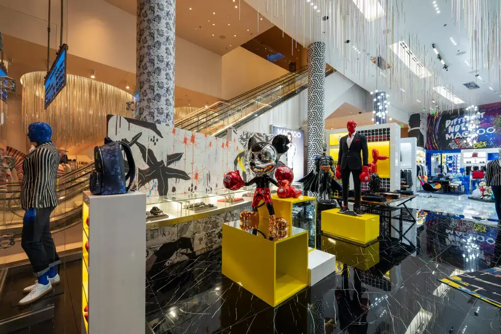 Look across the store from the mall entrance toward a black-and-white graffiti mural, yellow plinths and a tuxedo mannequin