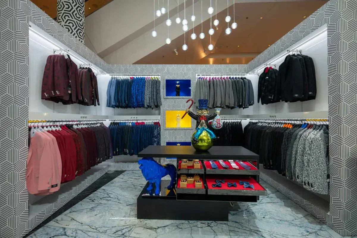 Suiting room lined with burgundy, pink and patterned sport coats around a centre case of silk ties and bow ties on red velvet