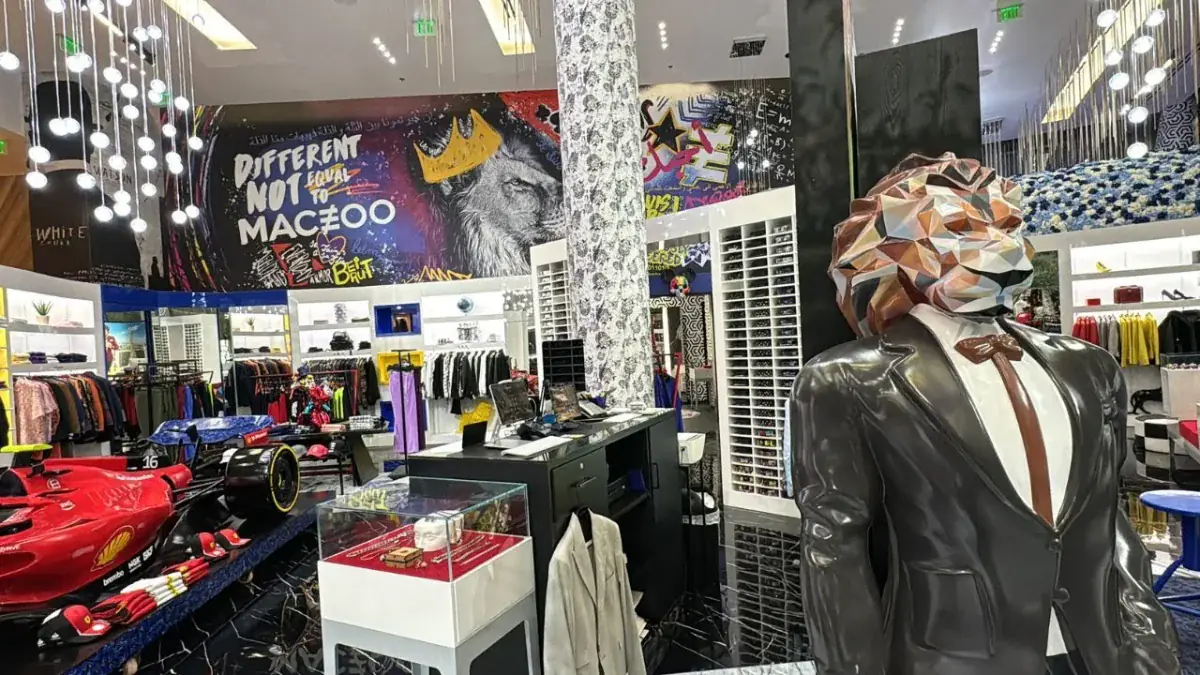 Geometric lion-head mannequin in a black dinner jacket standing beside a red Formula 1 show car under a graffiti mural