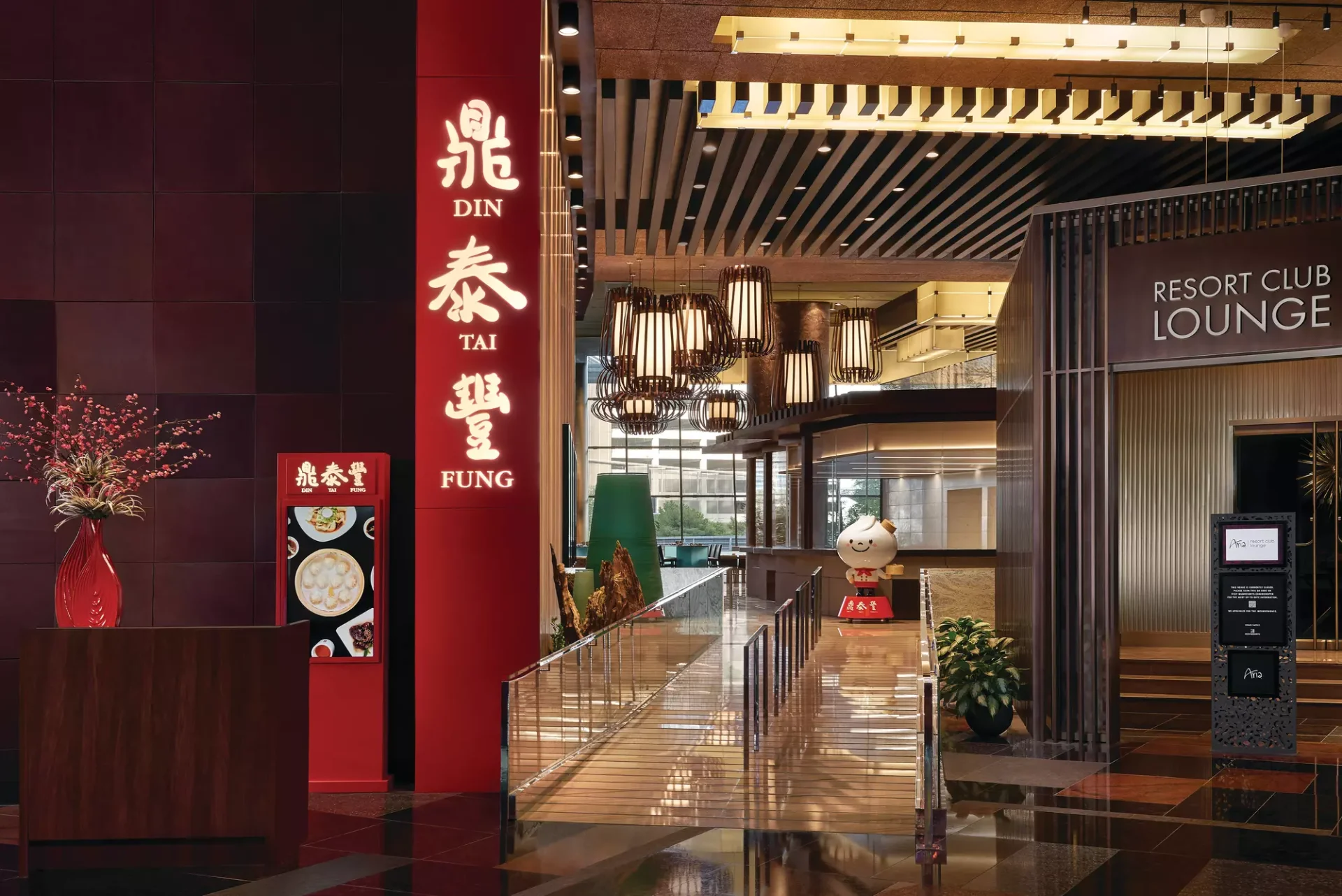 Illuminated red Din Tai Fung sign with gold Chinese characters at the ARIA Resort entrance, with the dumpling mascot and a walkway toward the Resort Club Lounge
