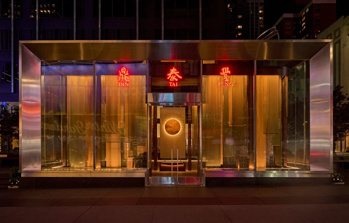 Brushed-metal and glass Din Tai Fung storefront facade lit with red neon signage at night