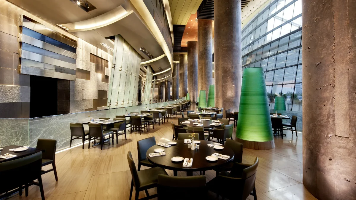 Soaring Din Tai Fung dining room with floor-to-ceiling windows, stone columns, green cone lamps, and round dark-wood tables