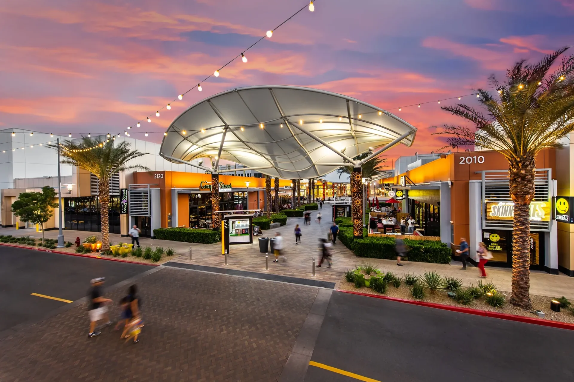 Open-air shopping promenade at Downtown Summerlin glowing under a sail canopy and string lights at sunset