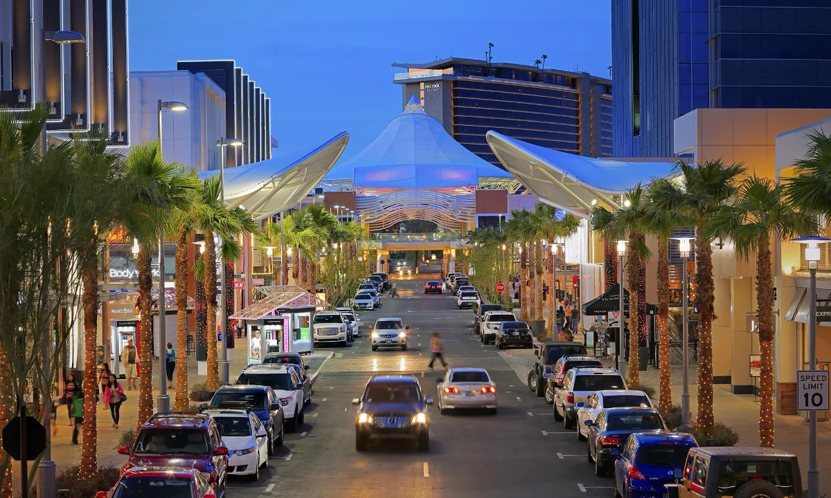 Tree-lined street at dusk leading toward the lit sail canopies and shops of Downtown Summerlin in Las Vegas
