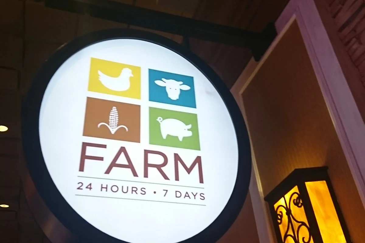 Close-up of the backlit round FARM sign with chicken, cow, corn, and pig icons above a 24 hours, 7 days tagline