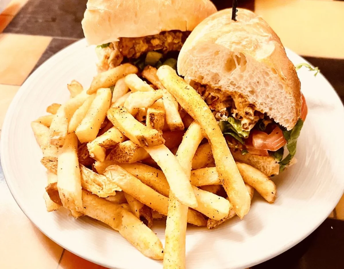 Fried chicken sandwich on a ciabatta roll with lettuce and tomato served with seasoned fries on a white plate at FARM