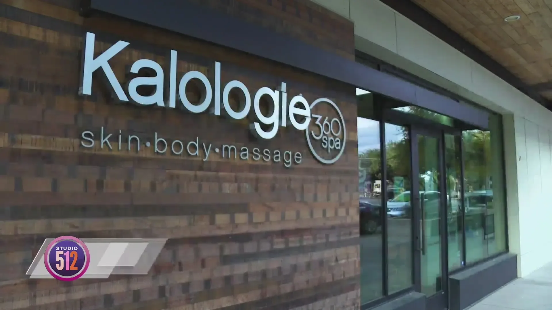 Exterior signage for Kalologie 360 spa reading skin, body, massage in white lettering on a wood-plank storefront wall beside the glass entrance doors