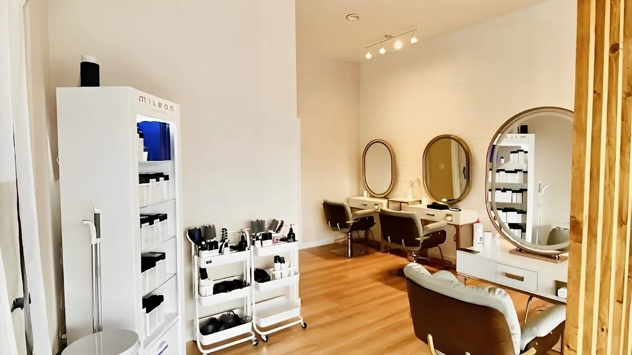 Bright Kalologie salon and retail area with round and oval mirrors over styling stations, cushioned chairs, blond wood flooring and shelves of Milbon skincare products