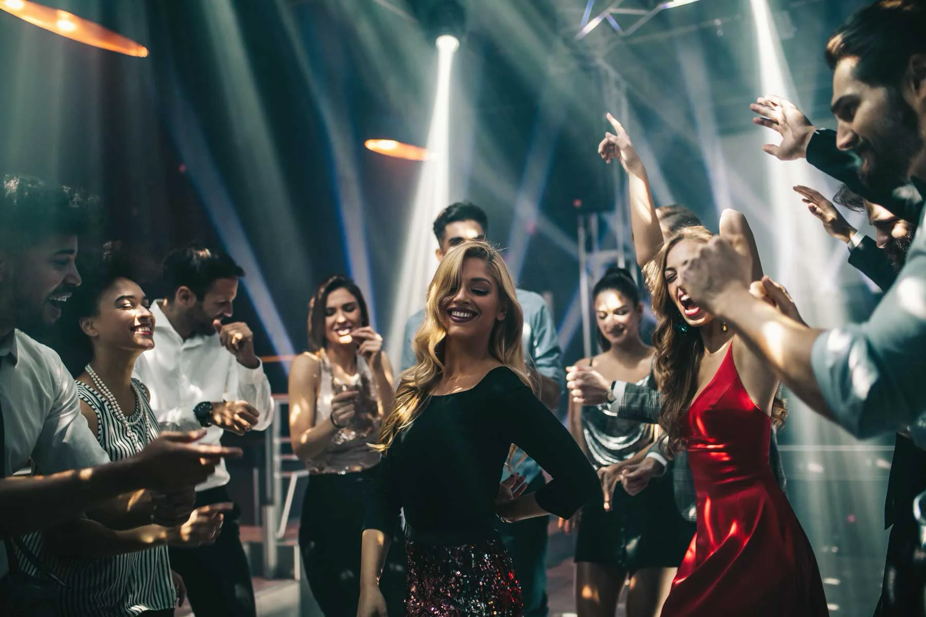 Crowd of stylishly dressed clubgoers dancing and laughing on a packed dance floor as white stage spotlights beam through haze at La Hacienda Nightclub