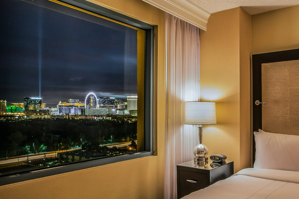 Suite bedside window framing the lit Strip skyline and High Roller wheel at night