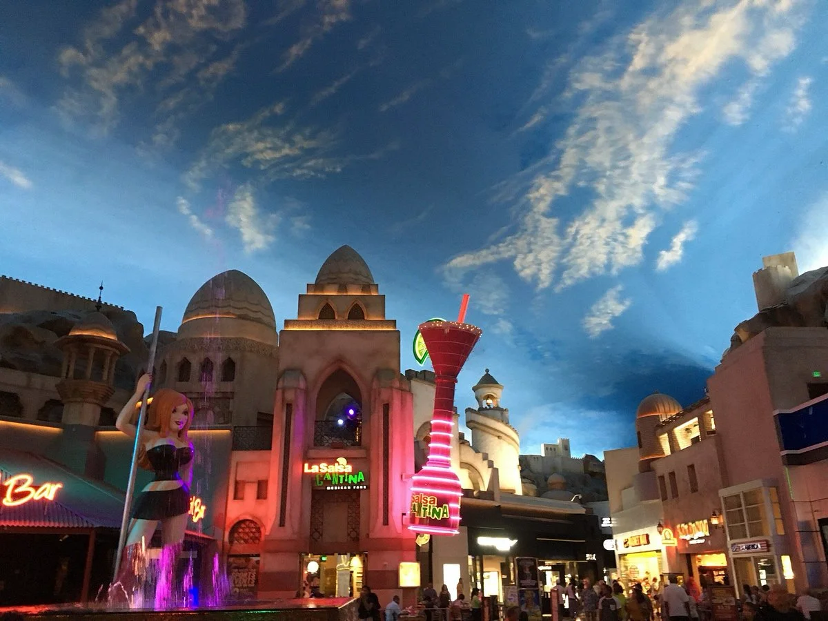 Desert-themed facades, neon signage, and a fountain at dusk inside the Miracle Mile Shops promenade