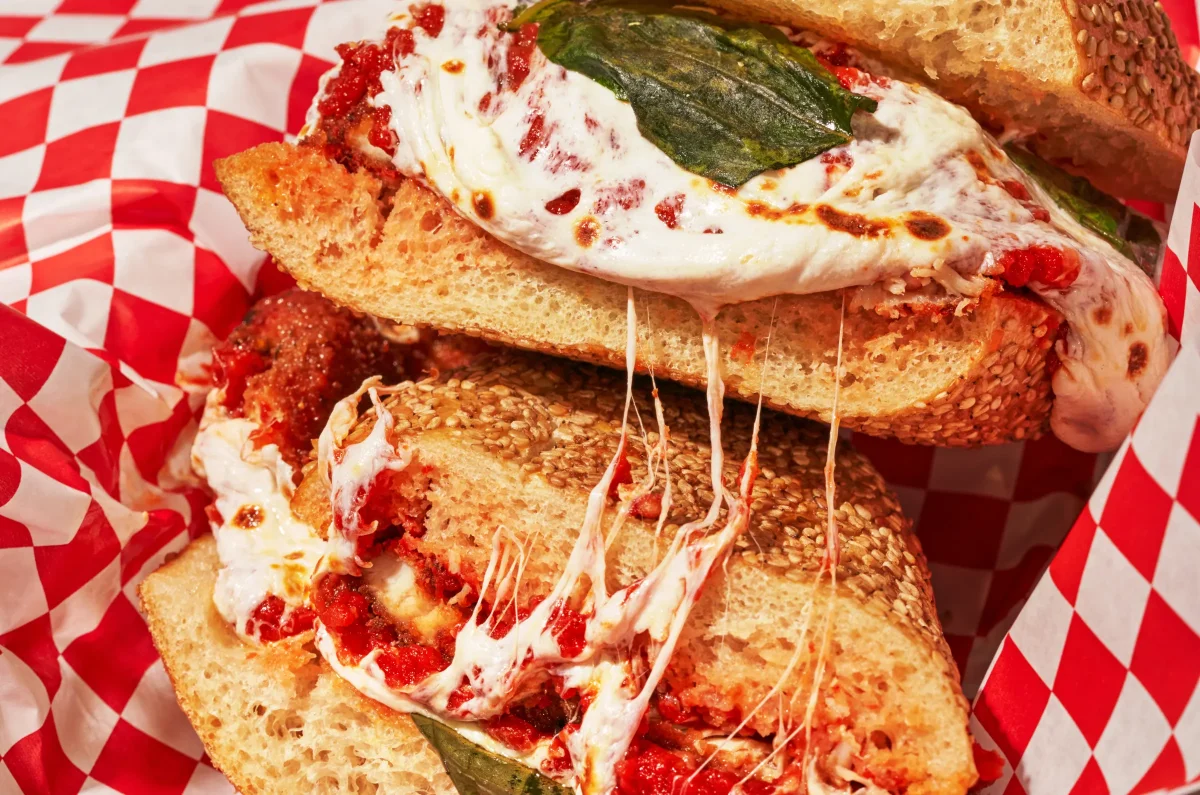 Chicken parmesan sandwich with melted cheese and marinara in a checkered basket at Proper Eats
