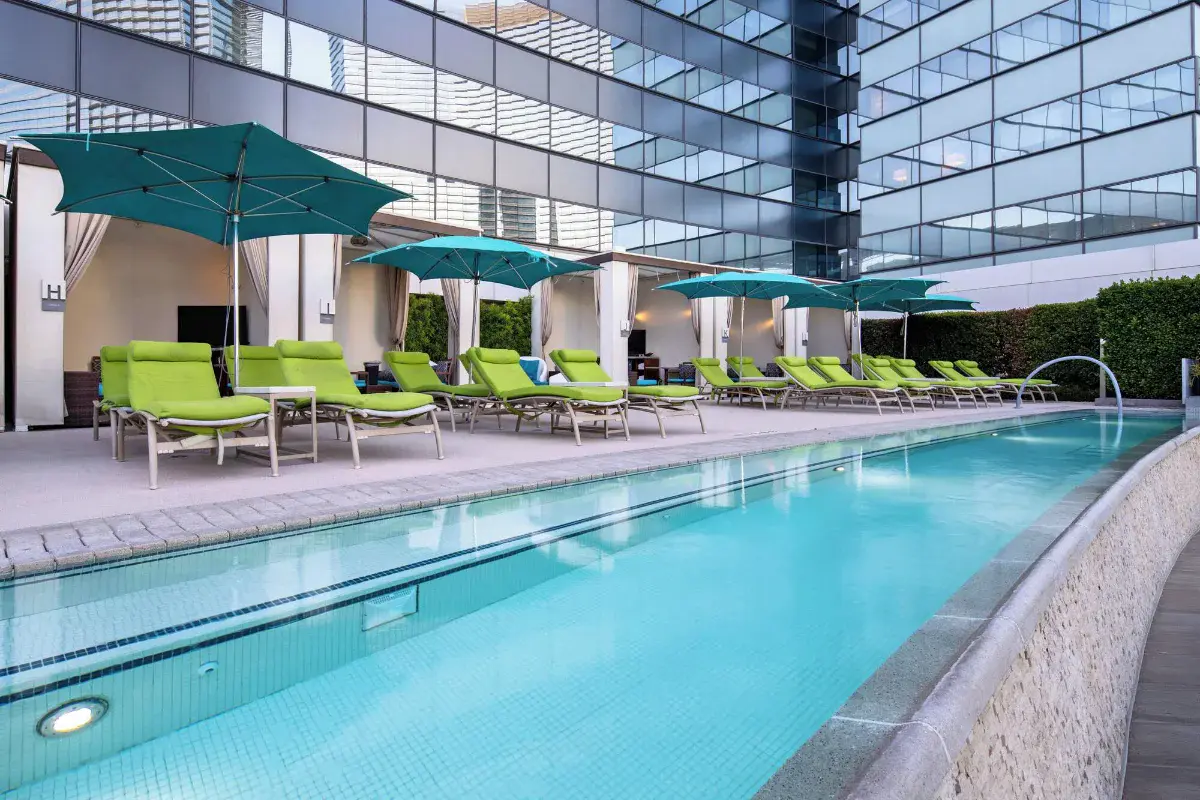 Outdoor pool with teal umbrellas and green loungers at Vdara