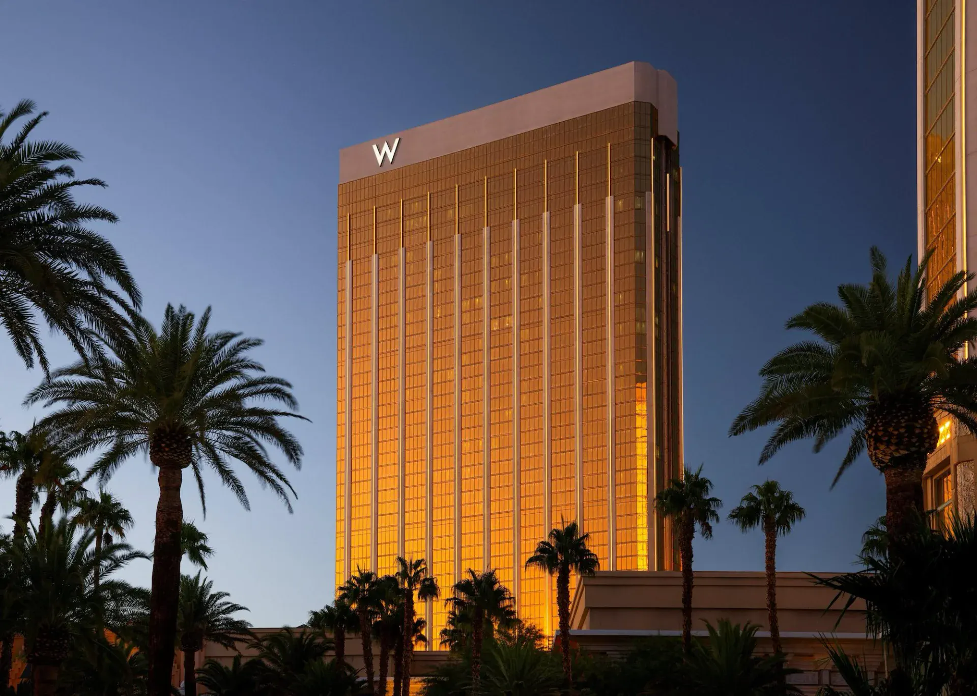 W Las Vegas gold tower at dusk framed by palm trees